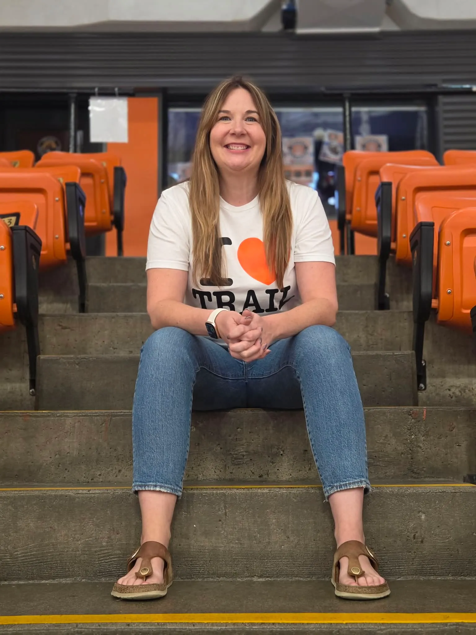 Bev Benson sitting on the steps between the orange seats at the Trail Memorial Centre