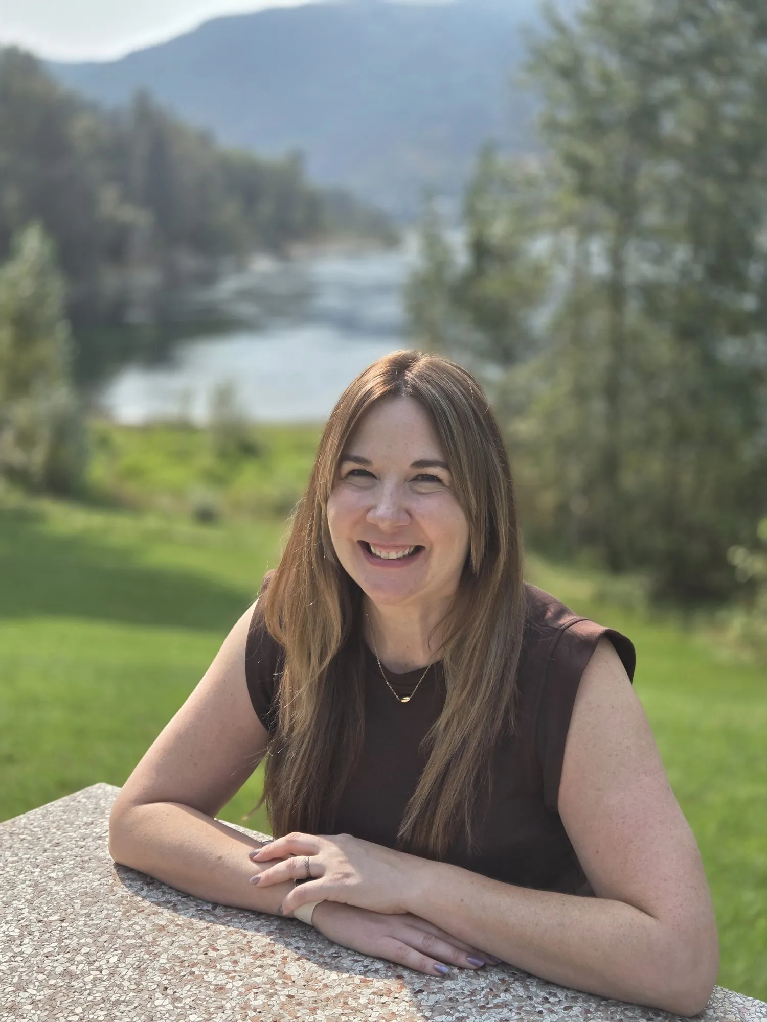 Bev Benson smiling at a picnic table beside the Columbia River